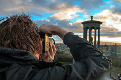 boy with camera taking photo of monument on calton hill edinburgh penguin and pia
