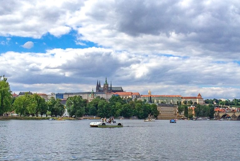 people in paddle boat on river with prague castle behind things to do in prague