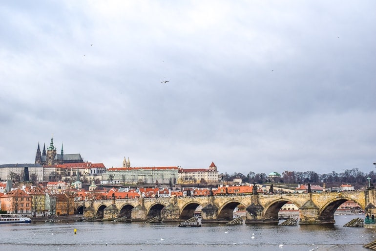 long bridge over river with castle on hill in prague