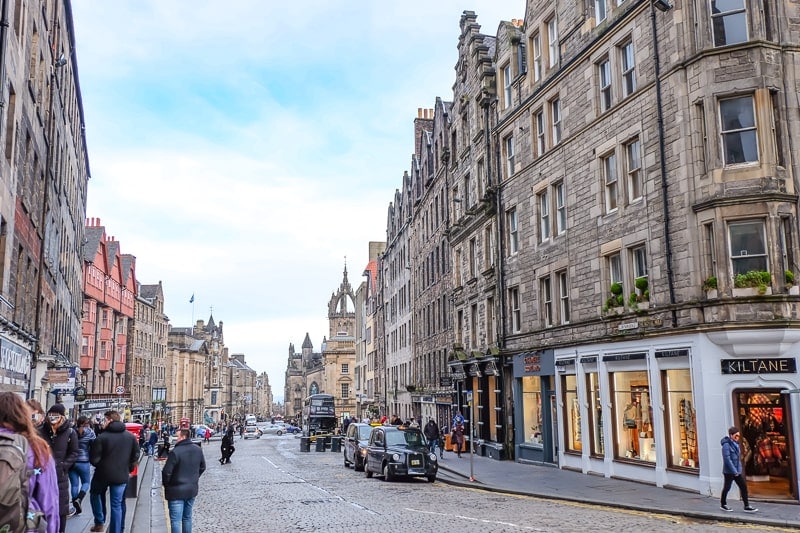 historic old street with shops and cars along royal mile edinburgh