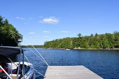 boat and wooden dock lookng over blue lake and green trees of ontario cottage rental