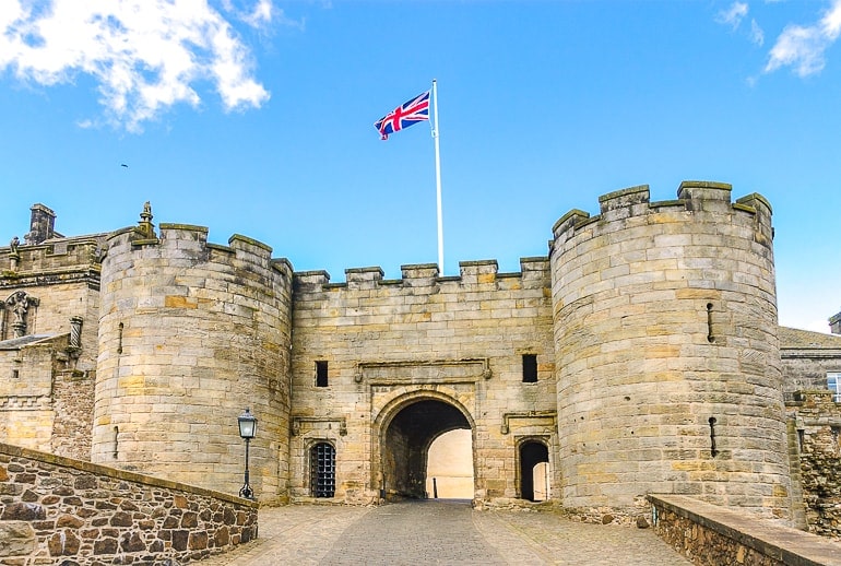old stone castle with entrance and british flag on pole atop.