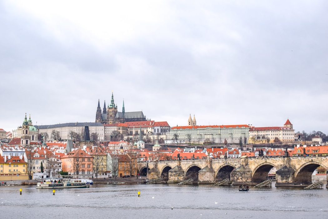 view of prague castle on hill with charles bridge across river in front