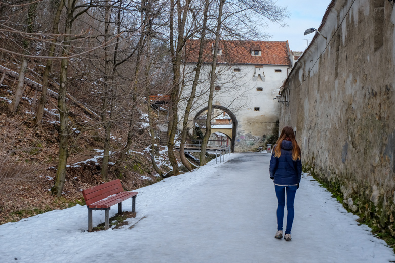 girl walking snowy path with bench and wall beside