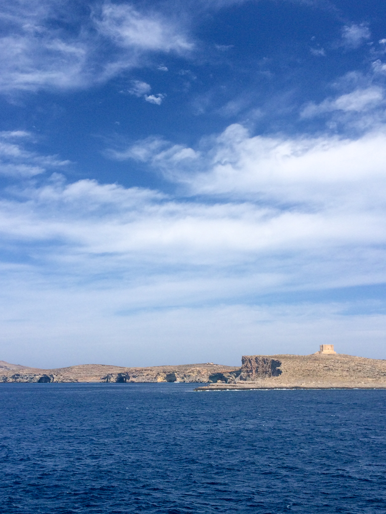 small tower on island of comino with blue sky and water