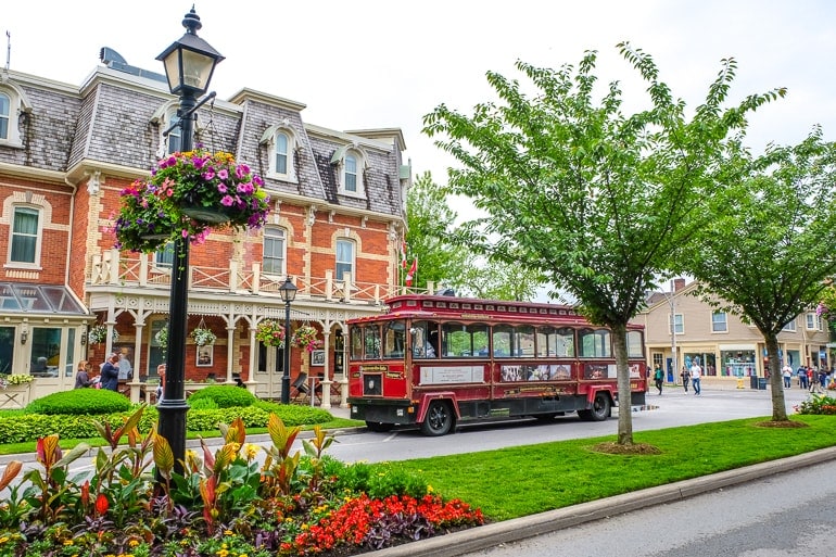 red trolley parked with old hotel behind and green gardens niagara on the lake