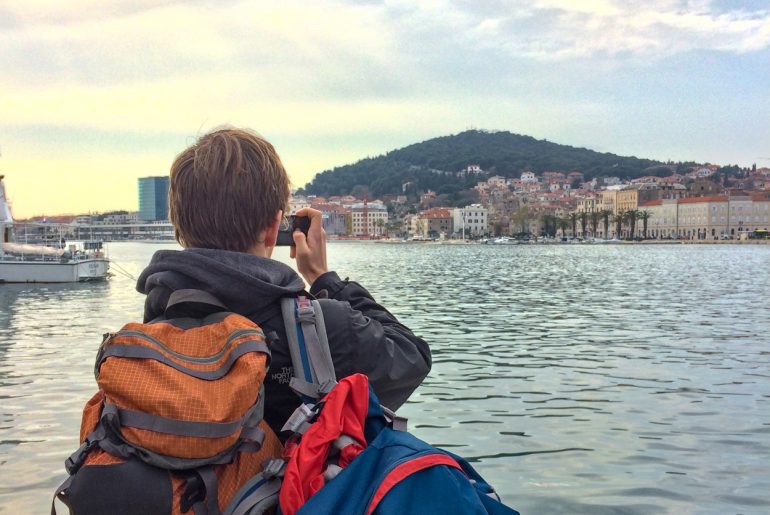 guy with backpacks on taking photo of harbour in croatia