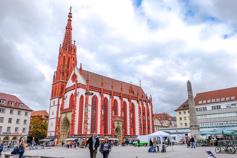 Rote und weiße Kirche mit Turm an Marktplatz mit Menschen in Würzburg
