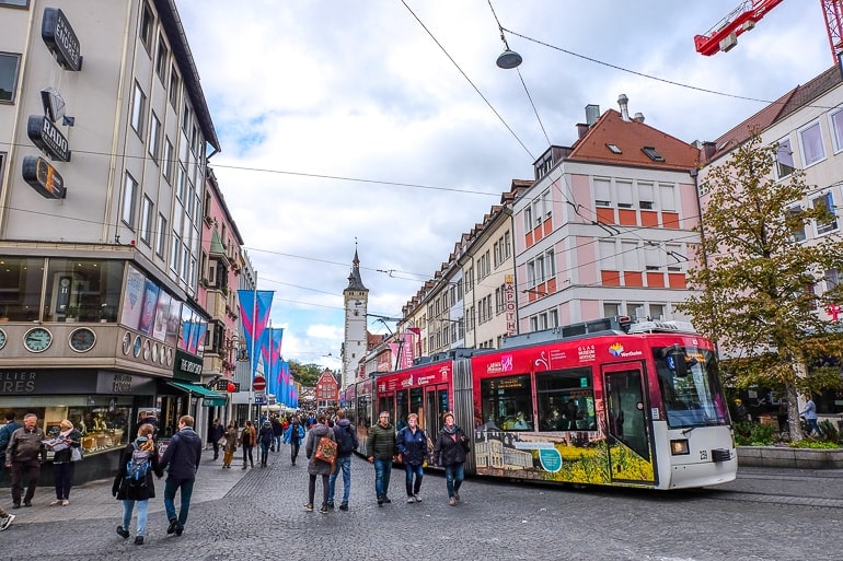 Straßenbahn fährt durch Altstadt von Würzburg, Menschen laufen auf Gehweg daneben