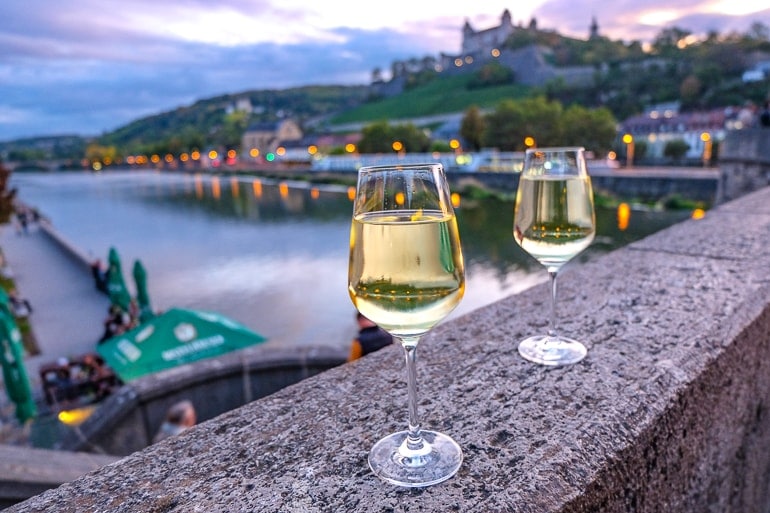 Zwei Weinglässer mit Weißwein auf Mauer von Alter Mainbrücke bei Dämmerung Würzburg Tipps