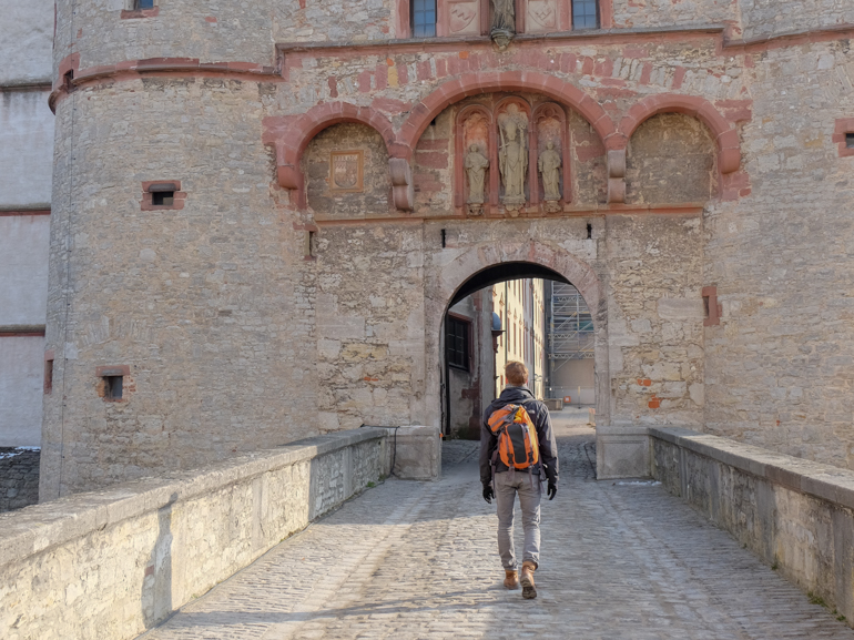 Mann mit orangenem Rucksack läuft auf Tor von Marienberg Festung Würzburg zu