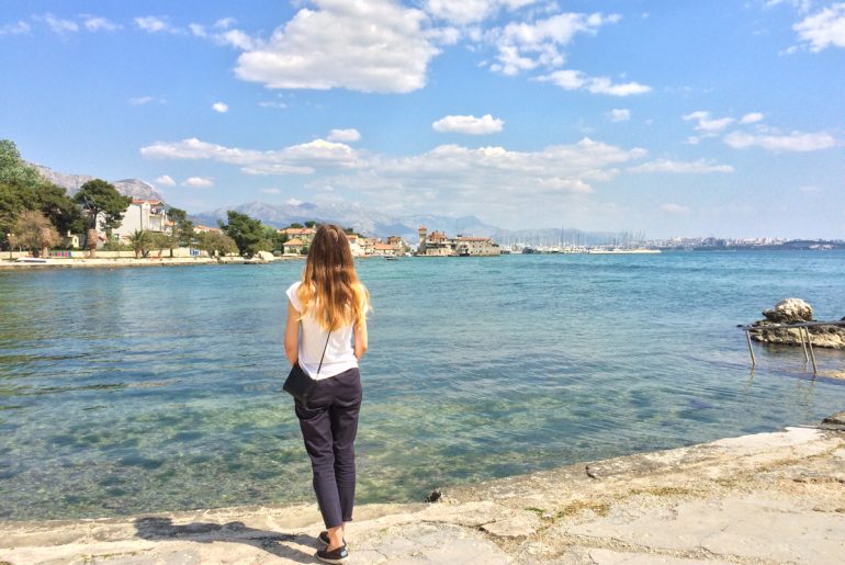 blonde girl standing on shoreline in croatia with blue water couple travel quotes