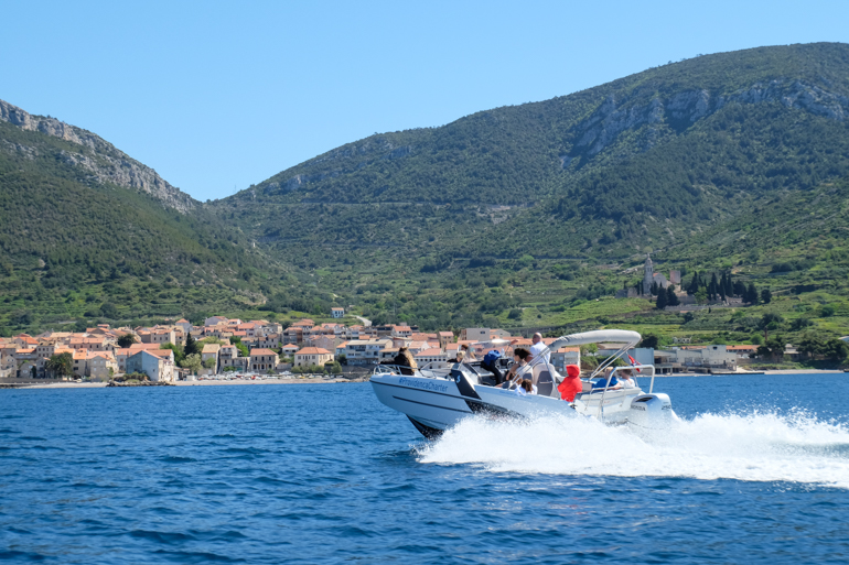 speed boat on blue ocean with old town and green mountain behind croatia island hopping