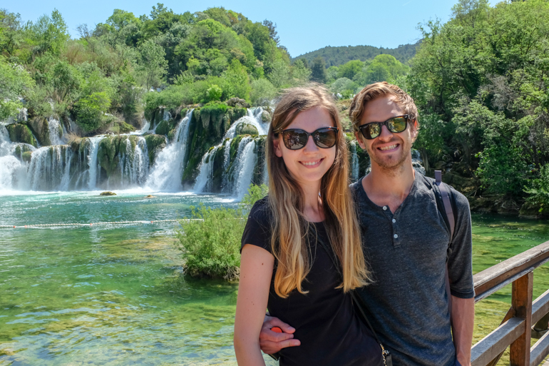 boy and girl with sunglasses pose in front of waterfall krka national park