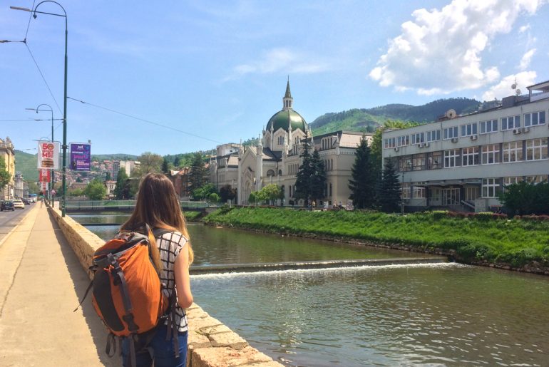 girl with orange backpack standing by river in sarajevo