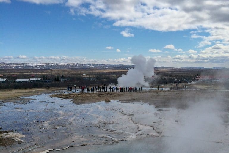 people stand around geyser in iceland planning a trip to iceland