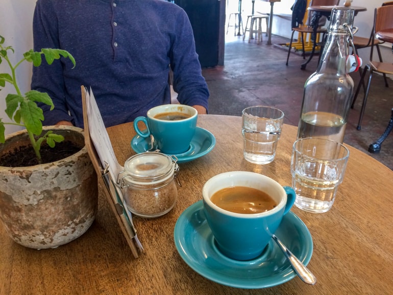 turquoise mugs and water glasses with menu on wooden table with green plant in coffee shop in edinburgh