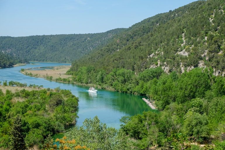 ferry on blue water through green trees in krka national park on croatia road trip