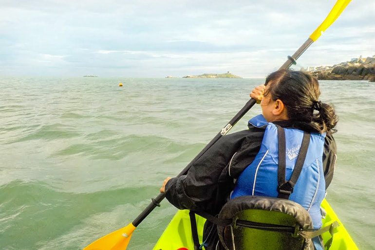 woman kayaking with paddle in green sea ireland travel tips