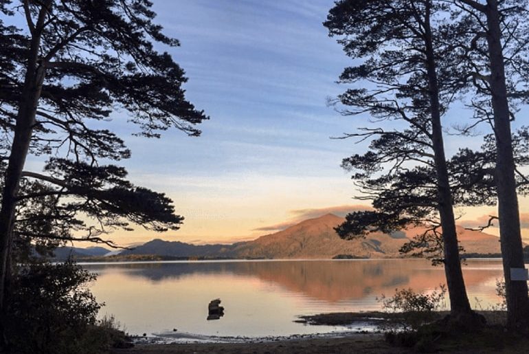 sunset and red trees with shadows on calm water at killarney national park ireland travel tips 