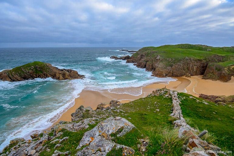 blue water and yellow sand beach with cloudy sky and green hills ireland travel tips