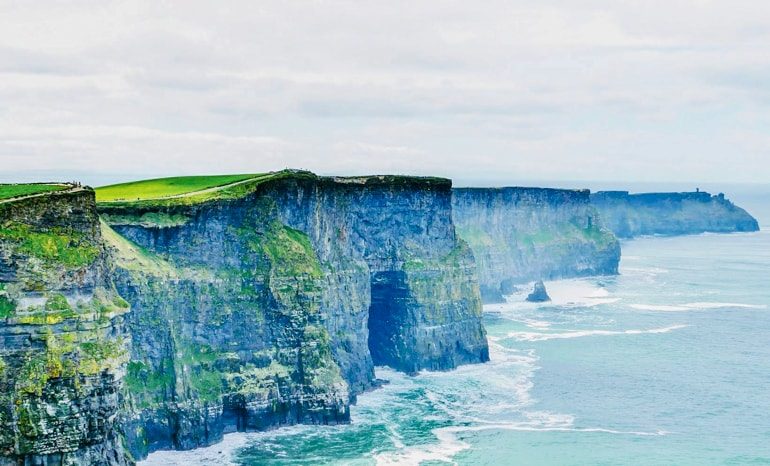 blue green cliffs of moher with waves crashing below in the distance ireland travel tips