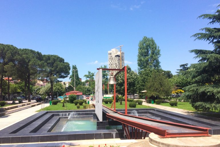 iron bell in green park with pond places to visit in tirana albania