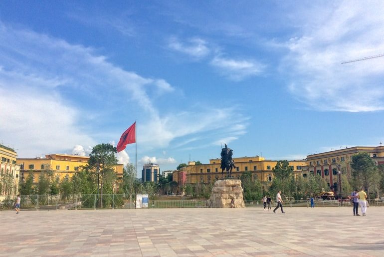 open square with statue and albanian flag and blue sky places to visit in albania