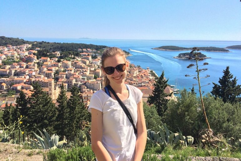 girl with sunglasses posing with old town croatia and sea behind her in hvar
