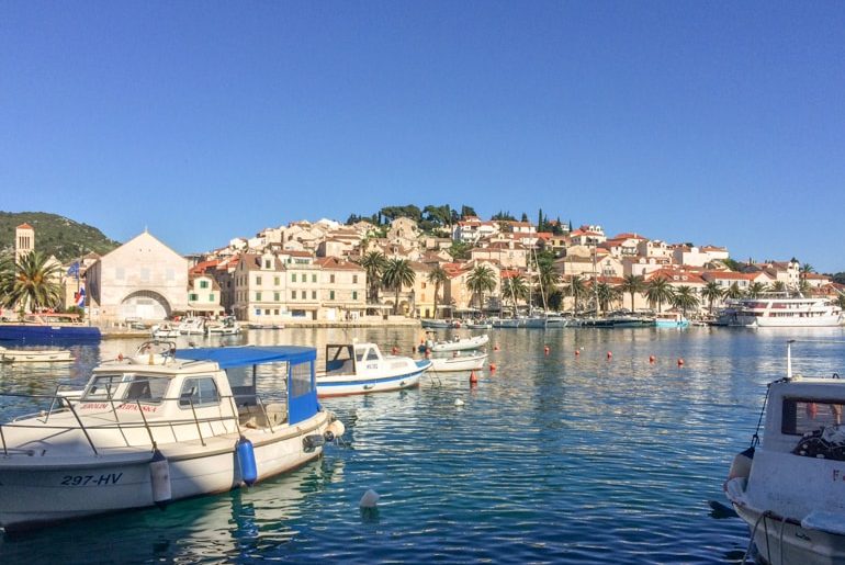 boats floating in the ocean with old town harbour and blue sky things to do in hvar