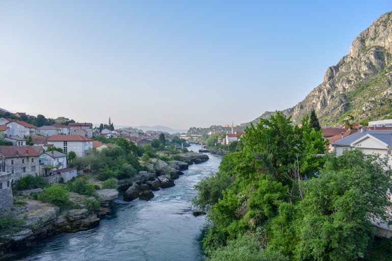 Blauer Fluss mit grünen Bäumen und alten Häusern in Mostar