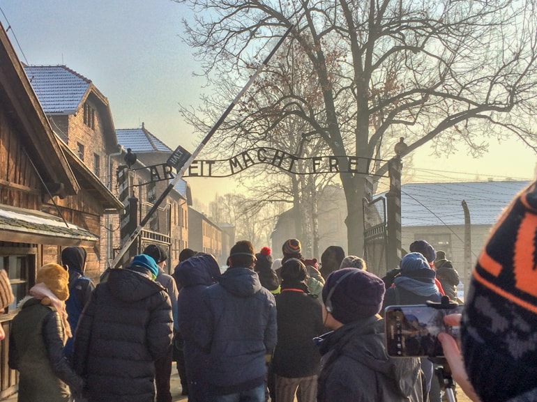 Menschen am Eingang des Konzentrationslager Auschwitz Arbeit macht Frei