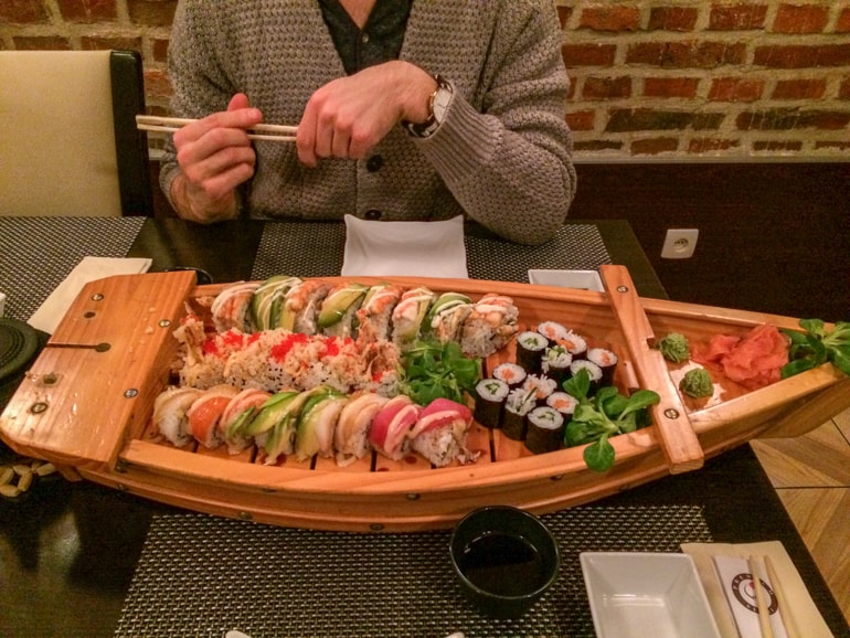 sushi rolls on sushi boat with man holding chopsticks