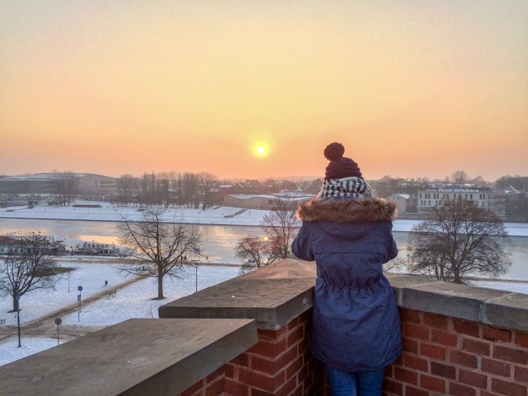 Frau mit Mütze vor orangenem Sonnenuntergang Krakau Polen