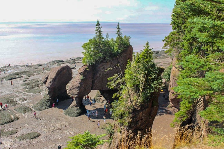 people walking under red rock formations in fundy national park canada sightseeing