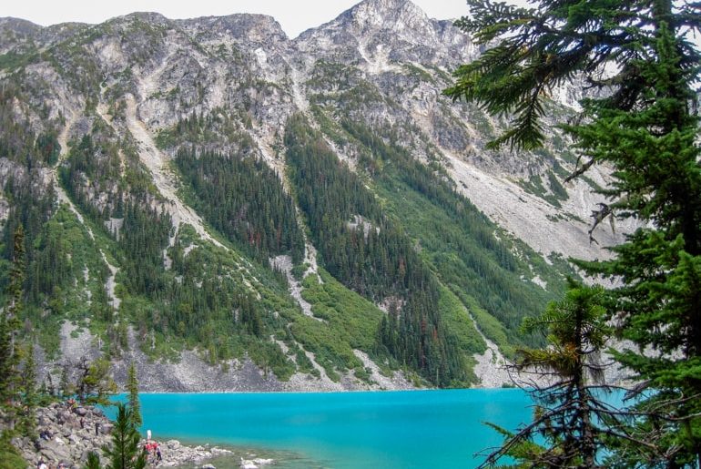 snowy and rocky mountains with blue lake and green pine trees below canada sightseeing
