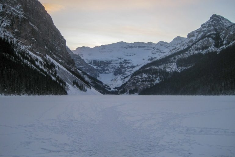 snow covered lake with rocky mountains in background in lake louise canada sightseeing