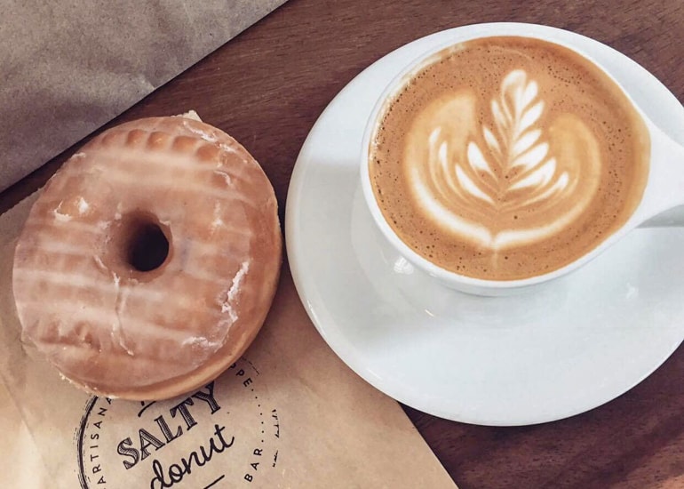 brauner Donut mit Kaffee in Tasse auf Holztisch Miami Reisetipps Salty Donut