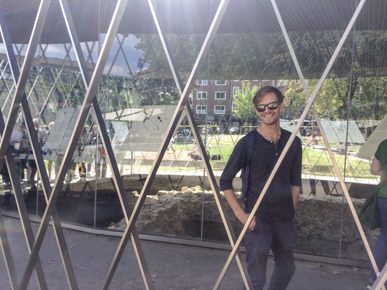 man in sunglasses behind metal supports with glass building behind.