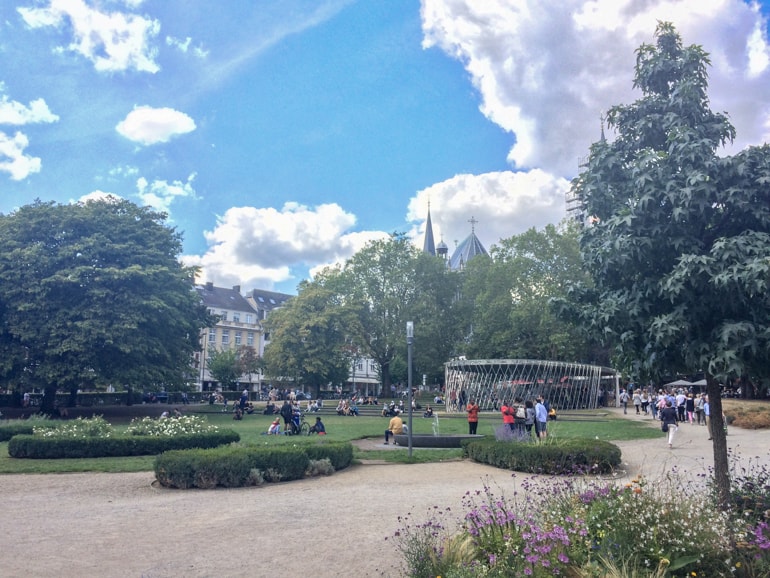 green park with buildings behind and cloudy blue sky above.