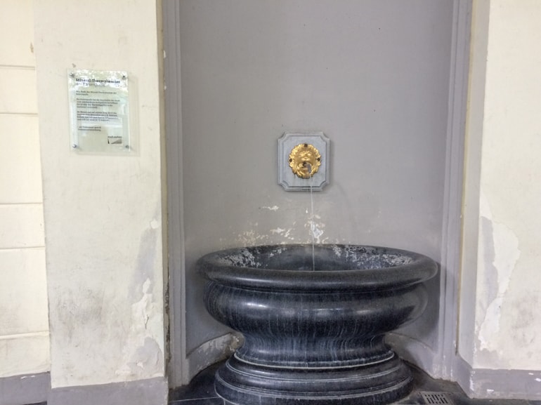 granite fountain with gold water tap sticking out of the wall.