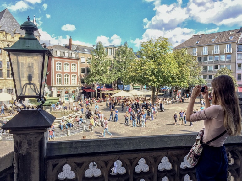 girl taking photo holding camera overlooking old square in german city.