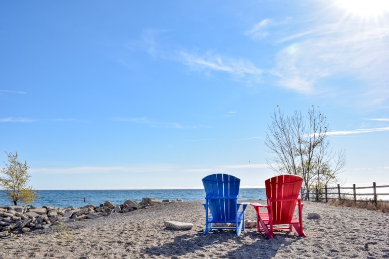 Blauer und roter Muskoka Stuhl am Strand im Herbst mit blauem Himmel Ontario Kanada