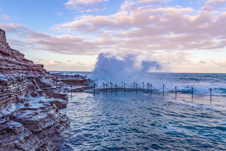 Ozean Pool mit spritzendem Wasser und pinkem Himmel Australien Attraktionen