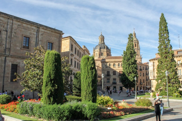 green trees in old spanish square with large domed building behind.
