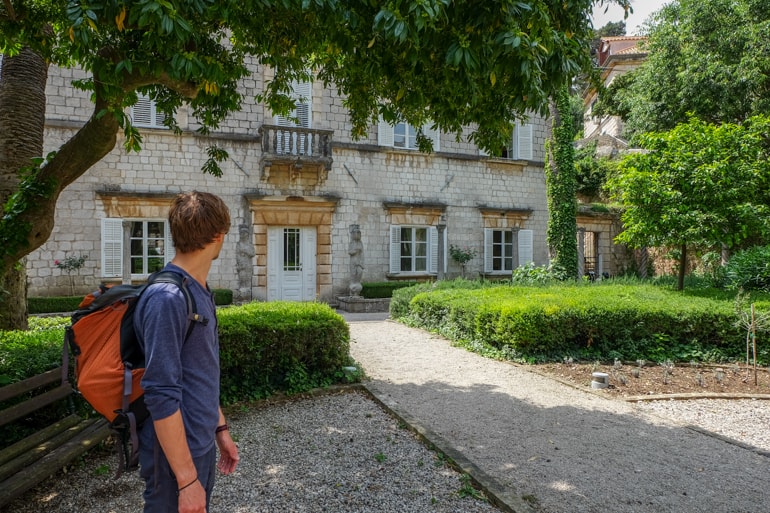 Mann mit Rucksack steht in Garten mit Haus im Hintergrund Dubrovnik Kroatien
