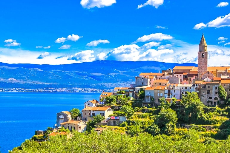 Dorf mit Turm und orangen Dächern bei blauem Ozean auf Insel Krk Kroatien