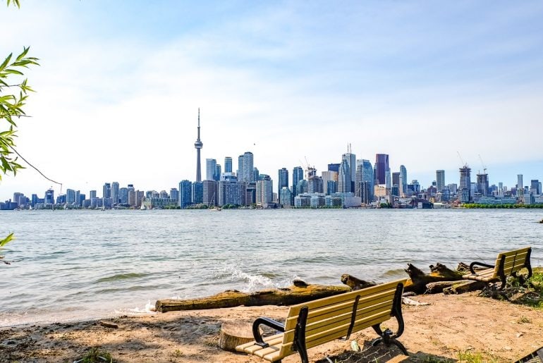 tall buildings of toronto skyline with beach and benches in foreground.