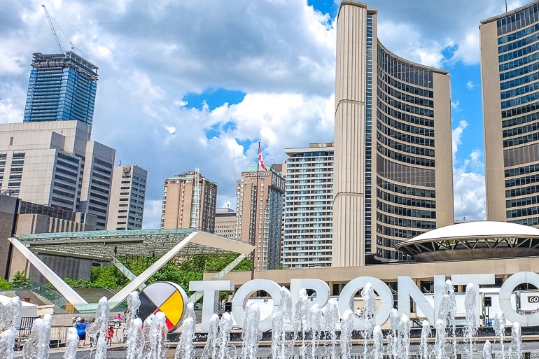 tall curved building with fountain and city sign in front in toronto with doubletree hotel behind