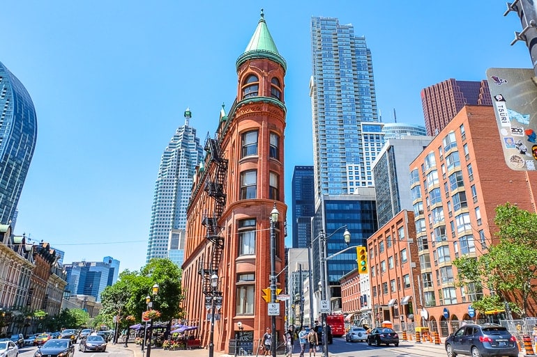 red flatiron building at street intersection with cars beside in downtown toronto.